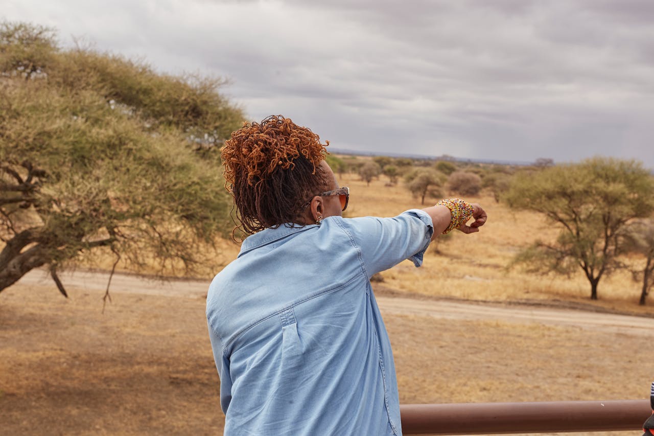 A woman in denim observes and points toward the vast savannah landscape.