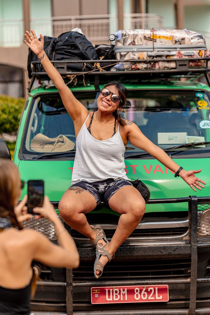 Happy woman sitting on a safari van enjoying an adventurous road trip outdoors.