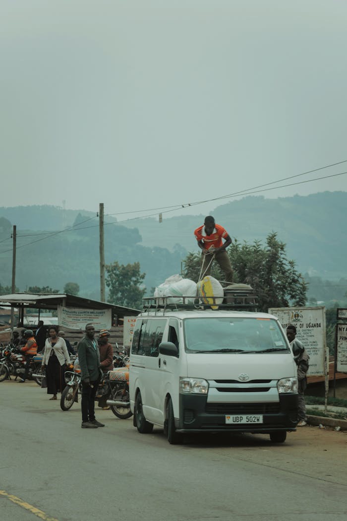 A busy roadside scene in Africa with people, vehicles, and cargo van under a cloudy sky.