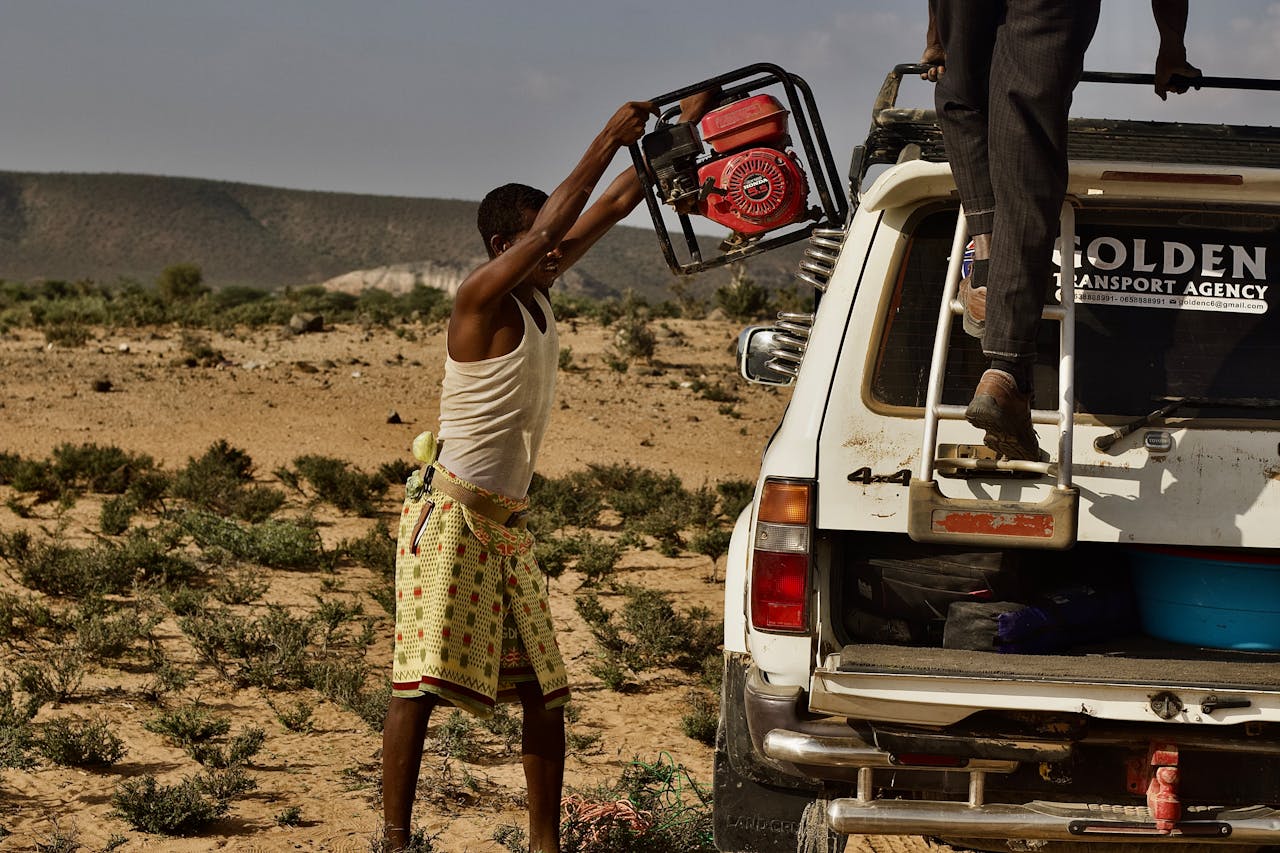 Two men outdoors loading a generator onto an off-road vehicle in a desert landscape.